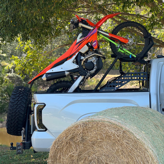 Motorcycle on a truck bed with a hay bale in the foreground, surrounded by trees.